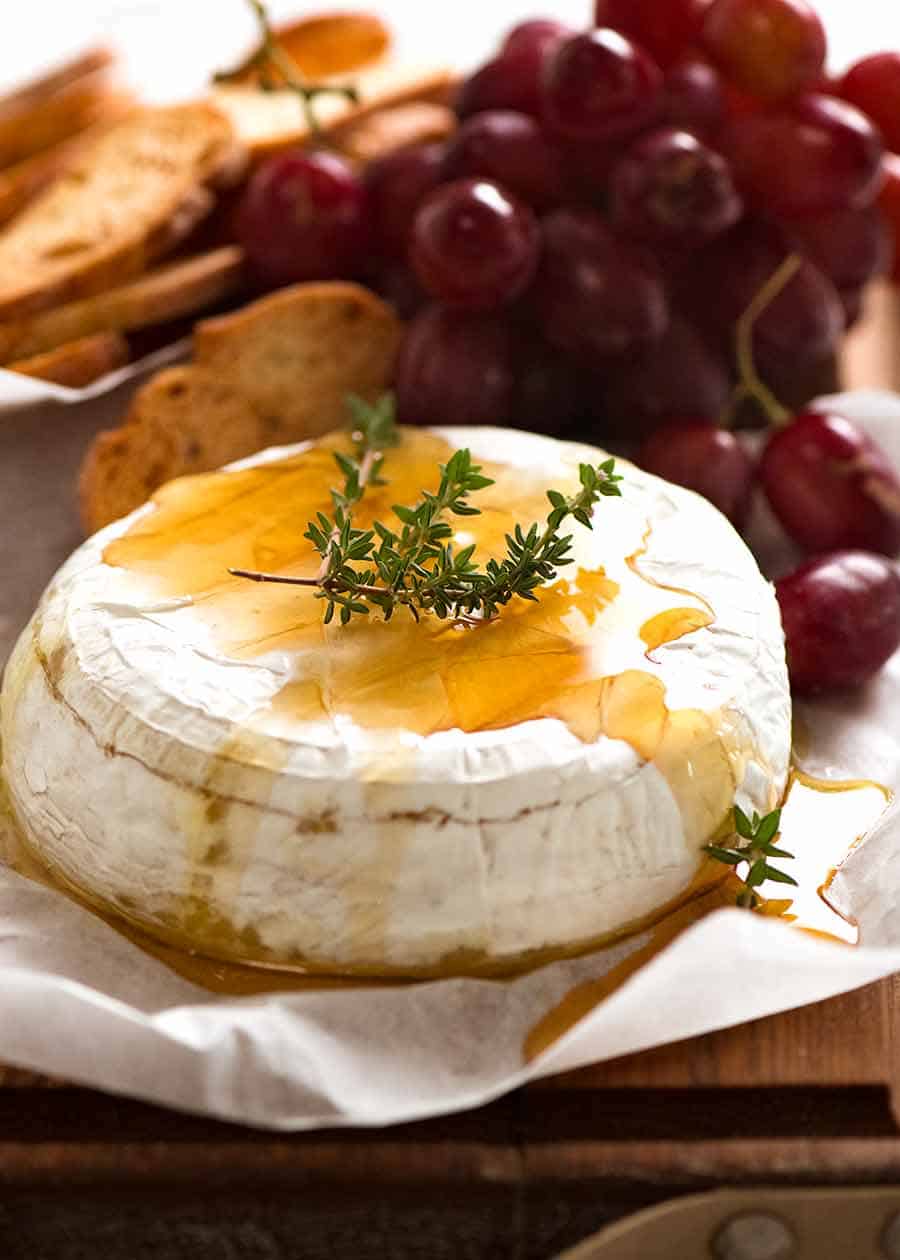 Photo of Baked Brie drizzled with honey garnished with fresh thyme, with crispy toasted bread and grapes