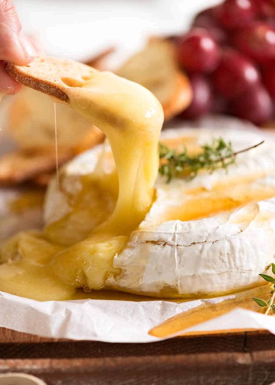 Close up of crispy toasted bread scooping up Baked Brie