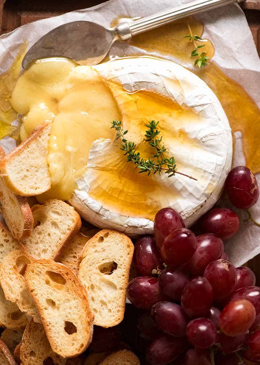 Overhead photo of Baked Brie drizzled with honey served with crispy toasted bread and grapes