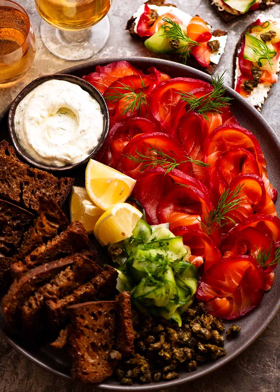 Beetroot Cured Salmon (Gin or Vodka, Salmon Gravlax) slices on a platter along with crispy bread and horseradish sauce for serving.