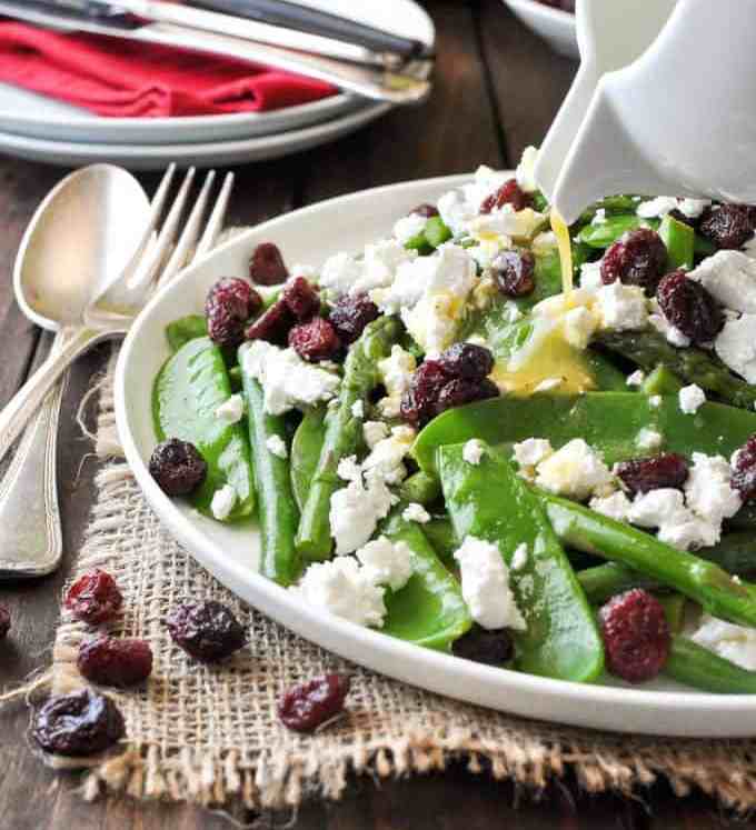 Dressing being poured over a Christmas Salad made with snow peas, asparagus, beans, feta and cranberries. Colours of Christmas!