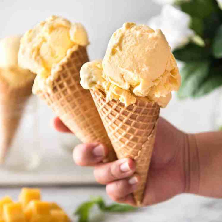 Two ice cream cones with mango ice cream held in a hand.