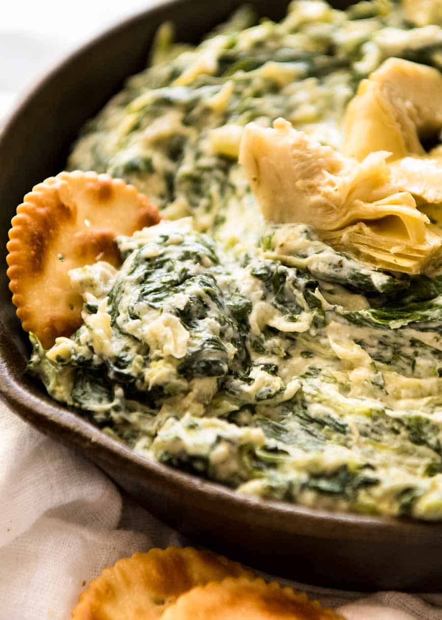 Close up of ritz cracker scooping up Spinach Artichoke Dip in a rustic black dish