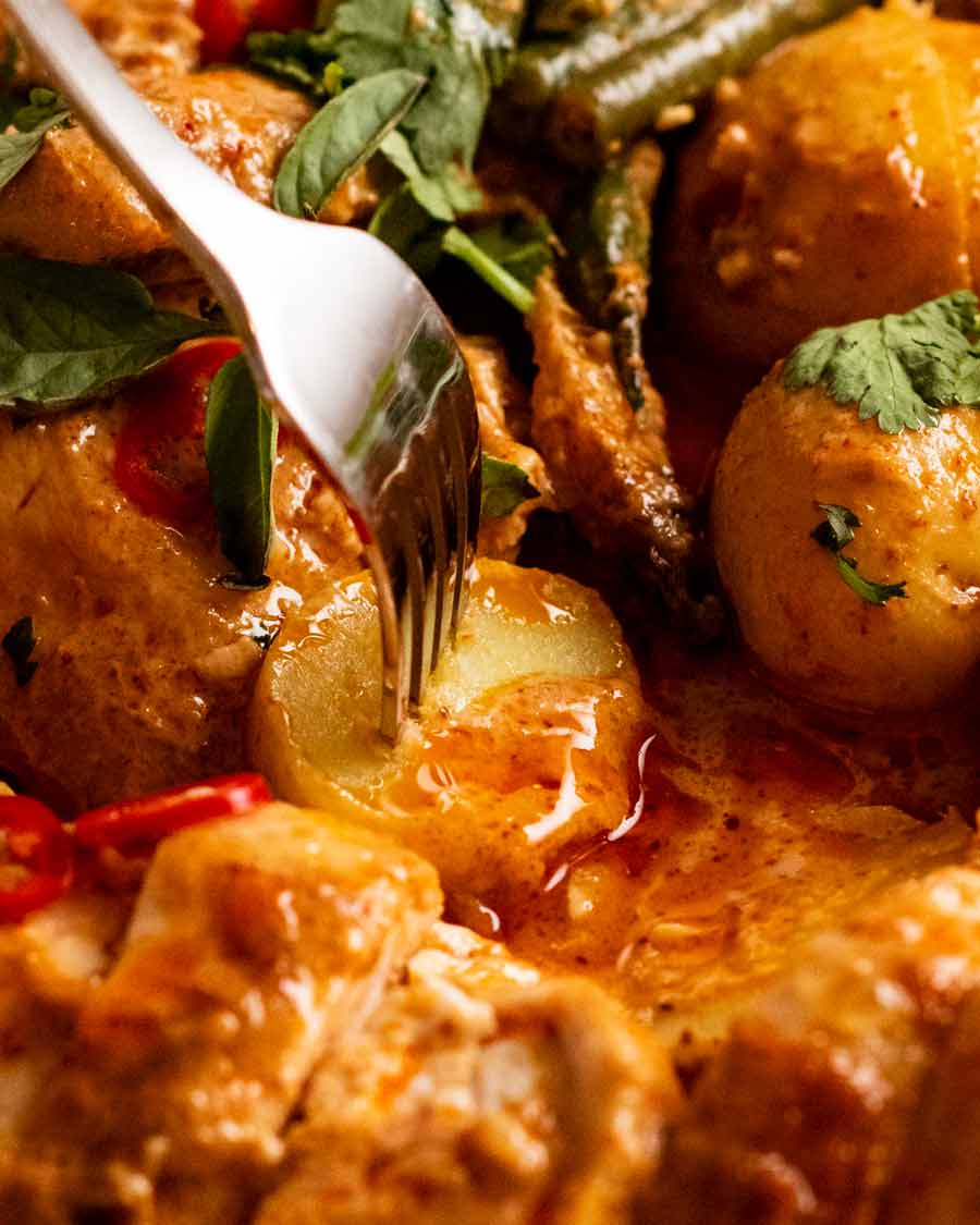 Fork picking up potato in Thai red curry pot roast chicken